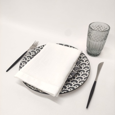 Conjunto de jantar com prato branco e preto, guardanapo branco, talheres pretos e copo transparente