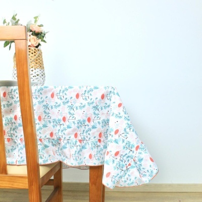 Toalha de mesa floral branca numa mesa de madeira com cadeira e vaso de flores.