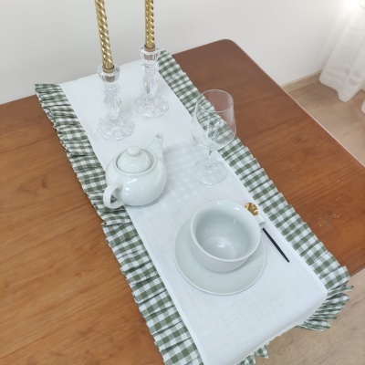 Conjunto de chá em cerâmica branca sobre caminho de mesa branco com bordas verdes, castiçais e copo em mesa de madeira