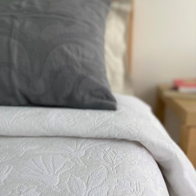 Cama com colcha branca texturizada e almofada cinza