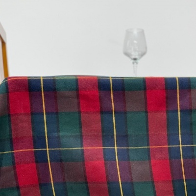 Toalha de mesa xadrez colorida com cadeira de madeira e copo de vidro ao fundo