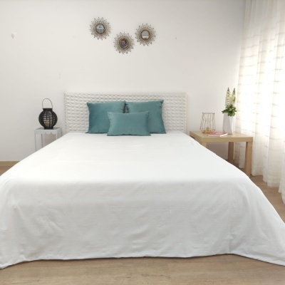 Cama com roupa de cama branca e almofadas azuis verdes em quarto com decoração minimalista