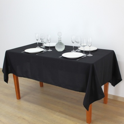 Mesa de madeira com toalha preta e louça branca, copos de cristal e decantador