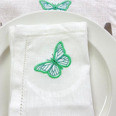 Pano de prato branco com bordado de borboleta verde, colocado num prato branco.