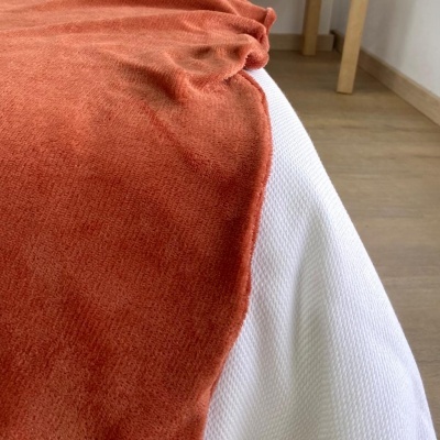 Cama com lençol branco e manta laranja em ambiente interior com chão de madeira