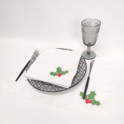 Conjunto de mesa com prato azul, guardanapo e base brancos com bordados verdes e vermelhos, copo cinza e talheres pretos