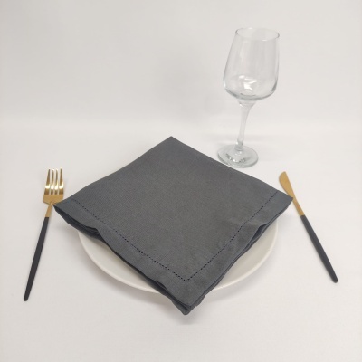 Talheres preto e dourado, guardanapo cinzento, prato branco, copo de vinho em vidro.