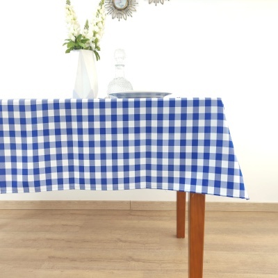 Mesa de madeira com toalha xadrez azul e branco e decoração com vaso e garrafa