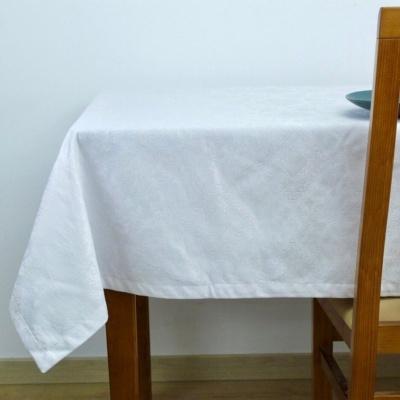 Toalha de mesa branca com padrão texturizado sobre mesa de madeira, cadeira ao lado e prato azul no canto