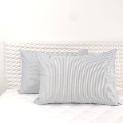 Duas almofadas azuis de riscas brancas sobre cama branca com cabeceira acolchoada