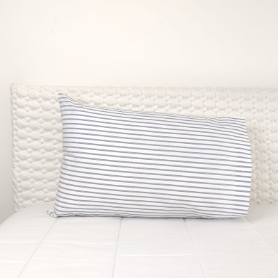 Almofada branca com riscas azuis sobre cama branca com cabeceira texturizada