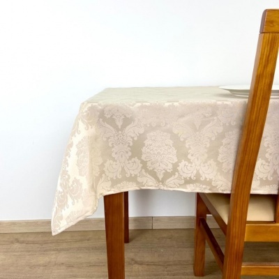 Toalha de mesa bege com padrão clássico em relevo numa mesa de madeira ao lado de cadeira de madeira