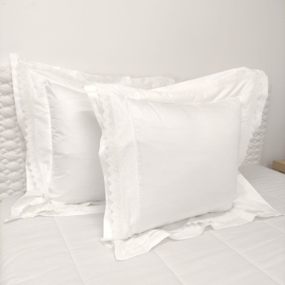 Três almofadas brancas com bordados delicados numa cama branca