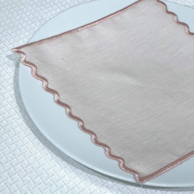 Guardanapo bege com acabamento ondulado rosado sobre prato branco