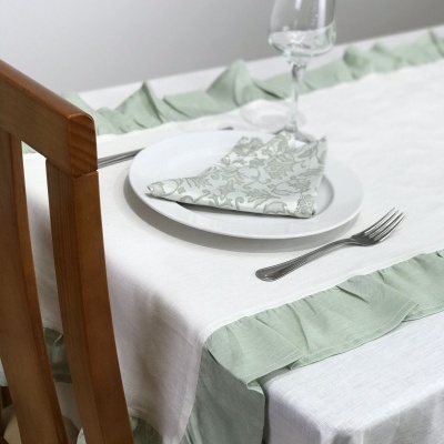 Mesa posta com toalha branca e verde, prato branco, guardanapo floral, garfo e copo transparente
