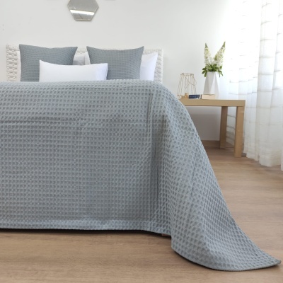 Colcha cinza texturizada com padrão colmeia sobre cama branca com almofadas cinza e brancas