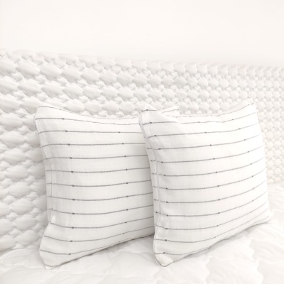 Duas almofadas brancas com riscas cinzentas em cama com cabeceira texturada branca