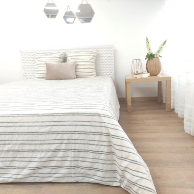 Cama minimalista com roupa de cama às riscas e mesa de cabeceira com vaso e candeeiro
