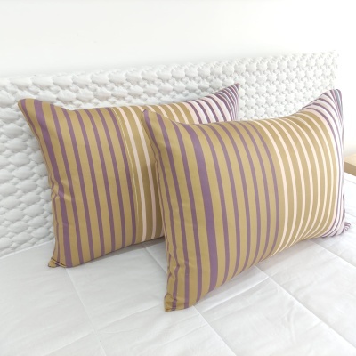 Almofadas listradas lilás e dourado sobre cama branca