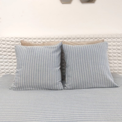 Cama com almofadas e lençóis azuis às riscas e cabeceira branca texturizada