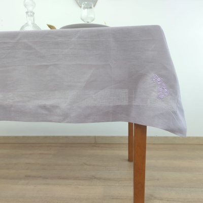Toalha cinzenta clara com bordado lilás numa mesa de madeira