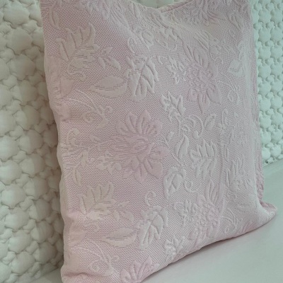 Almofada rosa claro com padrão floral em relevo junto a almofada branca acolchoada