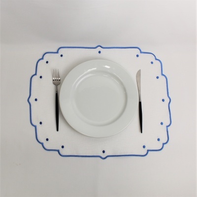 Prato branco com garfo e faca sobre individual branco com borda azul e pontos azuis