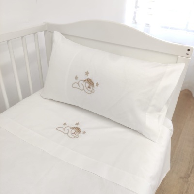 Lençol e fronha de bebé brancos com bordado de leão e estrelas bege numa cama branca