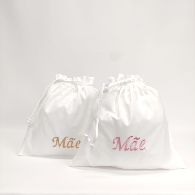 Dois sacos brancos de tecido com cordão e a palavra 'Mãe' escrita em rosa e dourado