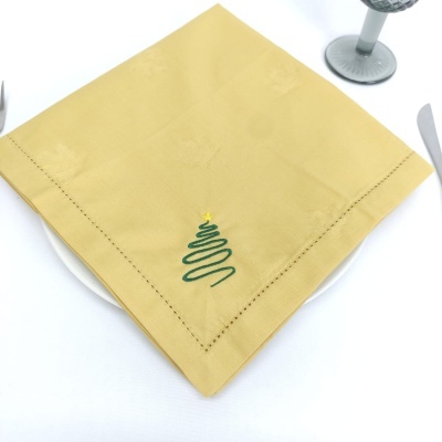 Guardanapo de tecido amarelo com bordado de árvore de Natal verde e estrela amarela numa mesa posta