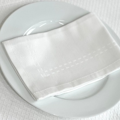 Toalha branca dobrada sobre prato branco com fundo branco texturizado