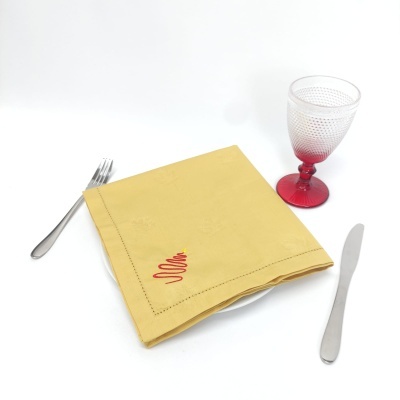 Guardanapo amarelo bordado sobre prato com talheres e copo vermelho