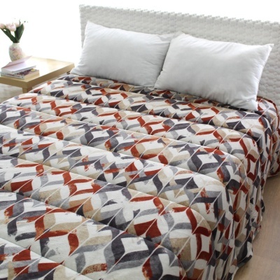 Colcha de cama colorida com padrão geométrico sobre cama branca com almofadas brancas e mesa de cabeceira com livros e vaso de flores.