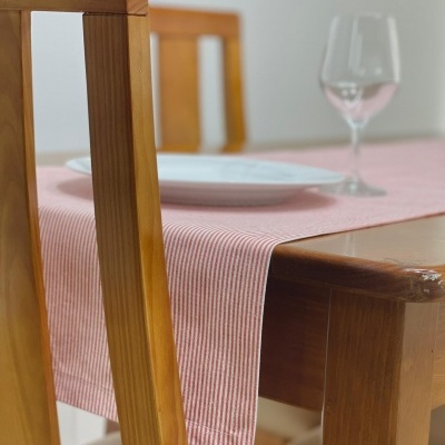 Mesa de madeira com toalha rosa riscada, cadeira de madeira, prato branco e taça de vidro