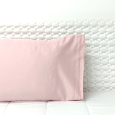 Almofada cor-de-rosa claro sobre colchão branco e cabeceira texturada branca