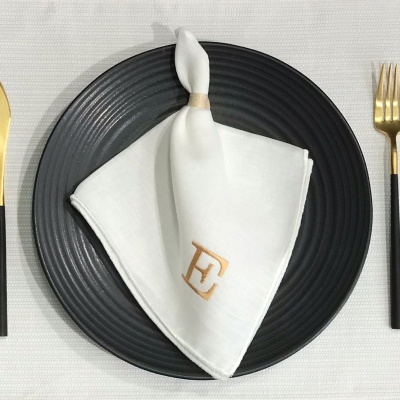 Conjunto de mesa com prato preto, guardanapo branco personalizado e talheres dourados com cabos pretos