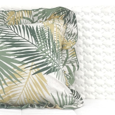 Almofada decorativa com padrão de folhas verdes e bege sobre sofá branco com parede texturizada branca ao fundo