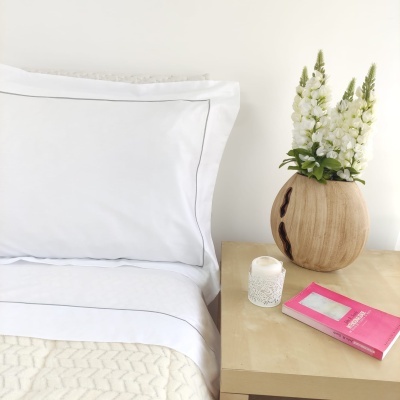 Cama com travesseiro branco, manta, vaso com flores, vela e livro na mesa de cabeceira