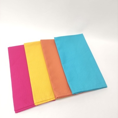 Quatro toalhas coloridas de tecido waffle em rosa, amarelo, laranja e azul sobre fundo branco