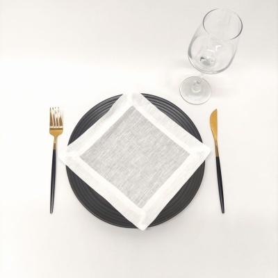 Mesa posta com prato preto, guardanapo cinza e branco, talheres preto e dourado, e copo de vinho transparente.