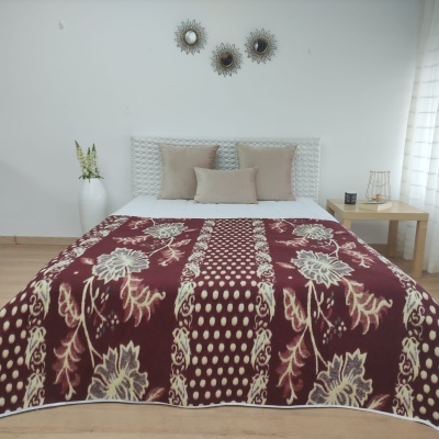 Cama com manta bordô e bege, almofadas bege, cabeceira branca e decoração simples na parede e mesa de cabeceira.