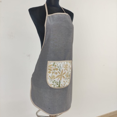 Avental cinza com bolso floral e moldura bege clara num manequim preto.