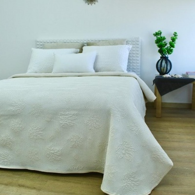 Cama com colcha branca texturizada, almofadas brancas, mesa de cabeceira com vaso azul e flores verdes, piso de madeira