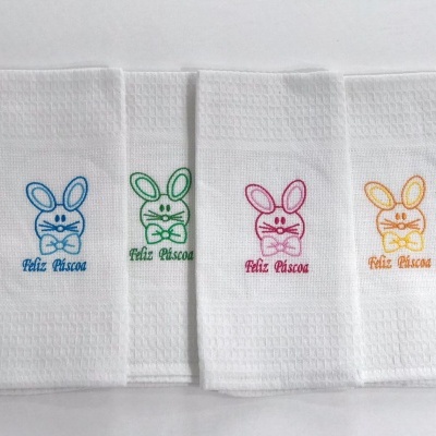 Quatro toalhas brancas com bordado colorido de coelho e texto 'Feliz Páscoa'
