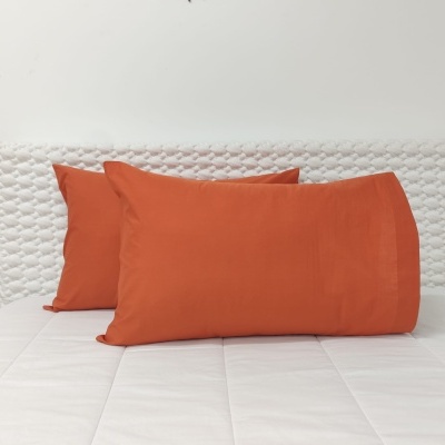 Três almofadas laranjas numa cama branca com cabeceira acolchoada