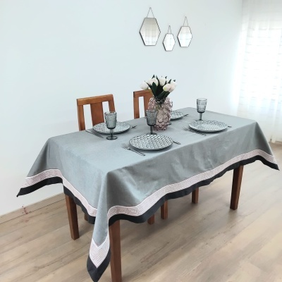 Mesa de jantar com toalha cinza, pratos com padrão, copos cinza e arranjo de flores