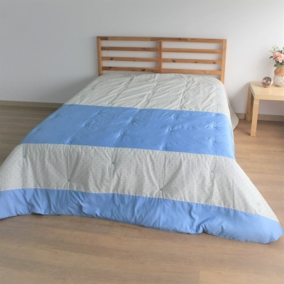 Cama de madeira com edredão azul e bege e mesa de cabeceira com flor