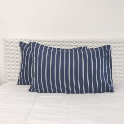 Duas almofadas com fronhas azuis e riscas brancas em cama branca com cabeceira acolchoada.