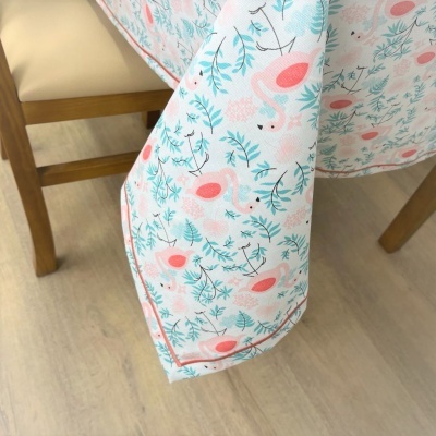 Toalha de mesa branca com padrão de flamingos cor-de-rosa e folhas azul-claras pendurada numa cadeira de madeira