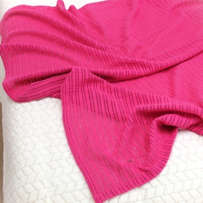 Manta rosa em malha com padrão de linhas perfuradas sobre superfície branca texturizada